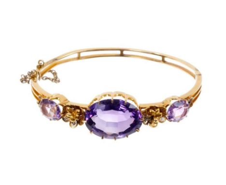 Victorian gold and amethyst hinged bangle with three oval mixed cut amethysts interspaced by two gold filigree flowers.