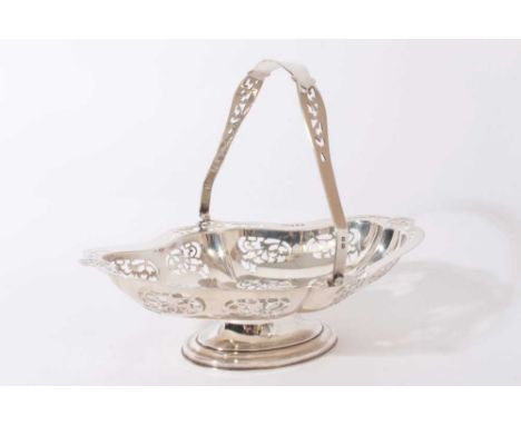 George V silver cake basket of shaped oval form with pierced scroll decoration, and swing handle, raised on oval pedestal foo