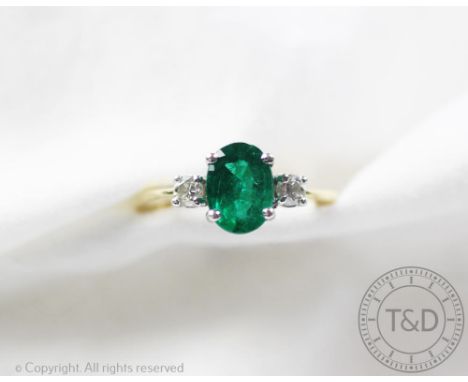 An emerald and diamond three stone ring, the central oval emerald flanked by a brilliant cut diamond to either side, all claw