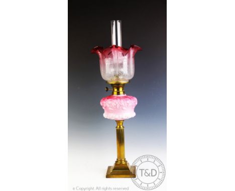 A Victorian brass oil lamp, with moulded pink glass reservoir decorated with flowers, on a fluted column and stepped square b