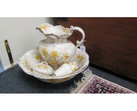 An Edwardian toilet set, comprising jug, basin, soap pot and brush holder, each transfer decorated with daffodils on a blush 