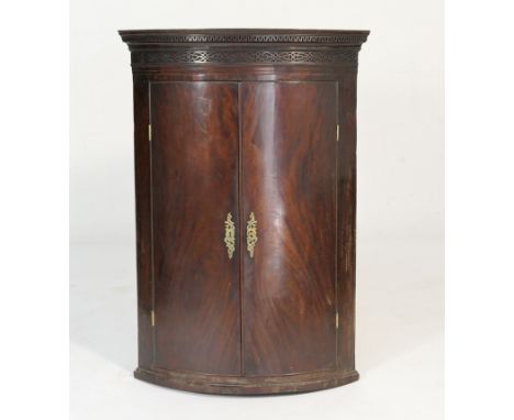 George III mahogany bow front hanging corner cupboard, circa 1800, dentil and blind fretwork cornice over two doors opening t