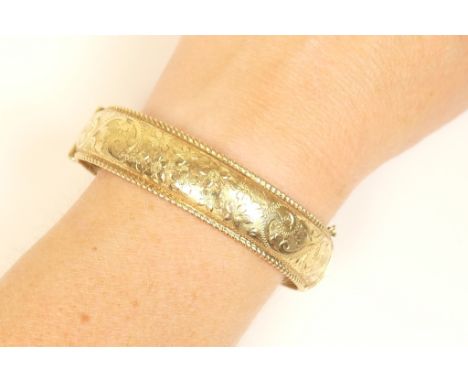 9ct gold hinged bangle, Birmingham 1967, engraved with foliate scrolls with a rope twist edge, interior size 60mm x 54mm, wei