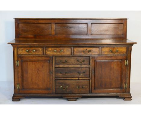 George III oak enclosed dresser, later triple recessed panel boarded back, the base fitted with four short drawers with brass