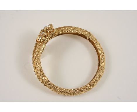 A 14CT. GOLD AND GEM SET DRAGON BANGLE realistically formed, the head and tail set with small diamonds, with ruby eyes.
