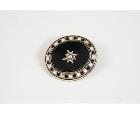 A BLACK ONYX AND GOLD BROOCH the oval-shaped section of onyx is mounted with a gold star set with a small pearl within a surr