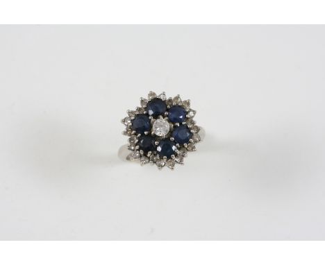 A SAPPHIRE AND DIAMOND CLUSTER RING centred with a brilliant-cut diamond within a surround of circular-cut sapphires and an o