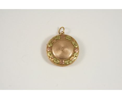 A TWO COLOUR GOLD LOCKET PENDANT of circular form, centred with engine turned decoration with a border of engraved foliate de