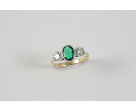 AN EMERALD AND DIAMOND THREE STONE RING the oval-shaped emerald is set with two circular-cut diamonds, in 18ct. gold. Size P.