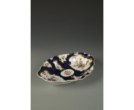 A WORCESTER FLUTED LOZENGE-SHAPED DISH painted in coloured enamels with flowers, within gilt cartouches, on blue scale ground