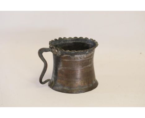 An antique Middle Eastern bath pitcher made of bronze or copper, featuring a flared base, a wavy top edge, and a single ornat