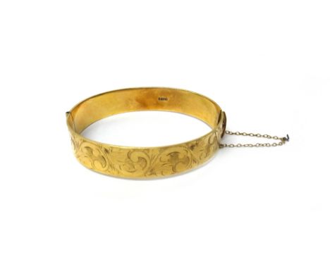 A 9ct gold oval hinged bangle, the front with feathered scroll engraved decoration, on a snap clasp, fitted with a safety cha