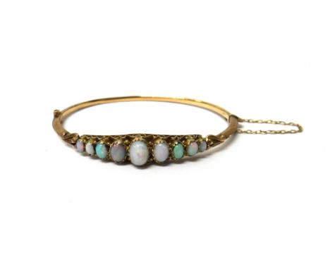 A 9ct gold and opal set oval hinged bangle, mounted with a row of nine oval opals graduating in size to the centre stone, the