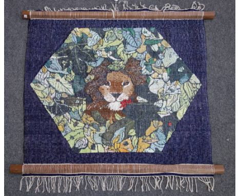 A needlework tapestry worked by Fleur Cowles, depicting a lion's head in a hexagonal flower filled panel, blue border, signed