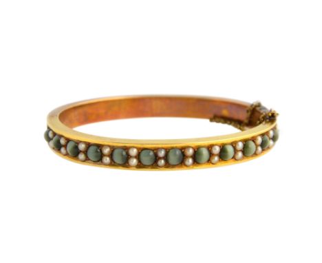 A Victorian gold, cat's eye and seed pearl set oval hinged bangle, the front mounted with a row of cat's eyes alternating wit