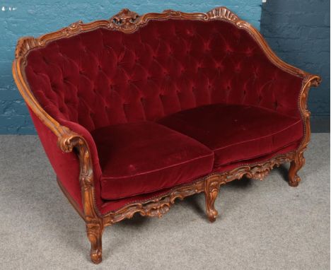 A carved mahogany two seat sofa. With red deep buttoned and studded upholstery.  Tear to the base.