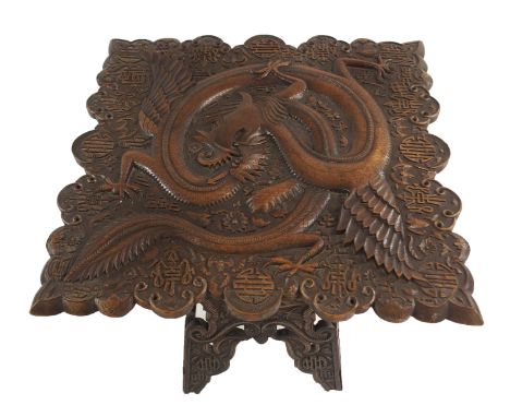 A CHINESE HARDWOOD OCCASIONAL TABLE carved in high relief with a dragon amongst precious symbols on a hinged four-panel base 