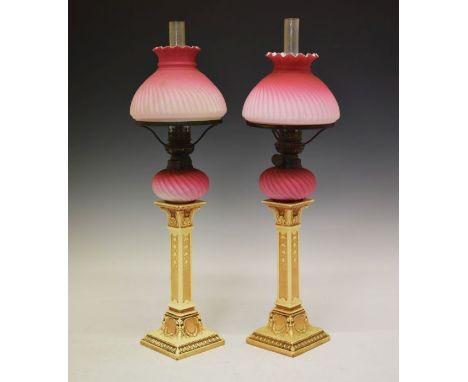 Pair of late 19th/early 20th Century candlestick oil lamps, each having a wrythened pink satin glass reservoir and shade, the