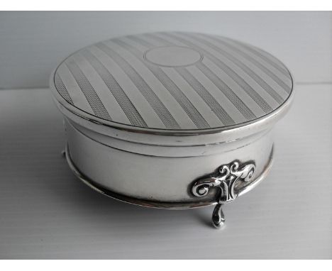 An Edwardian silver circular trinket box with hinged lid, fabric-lined interior, engine-turned design to top on three hoof fe