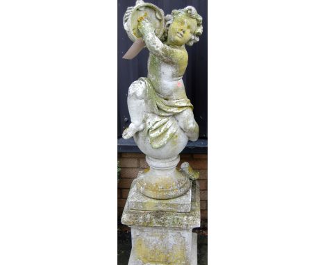 A reconstituted stone garden figure of a seated cherub playing a tambourine, raised on further square section pedestal (a/f t