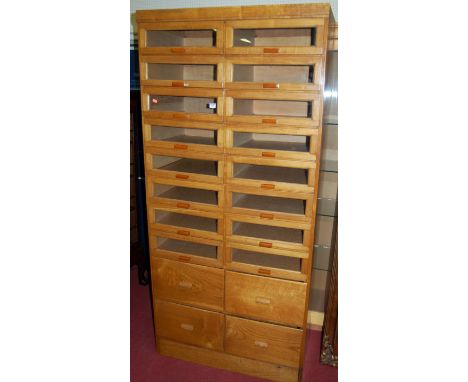 A 1930s light oak freestanding haberdashery cabinet, having multiple glazed drawers over four further short drawers, with amb