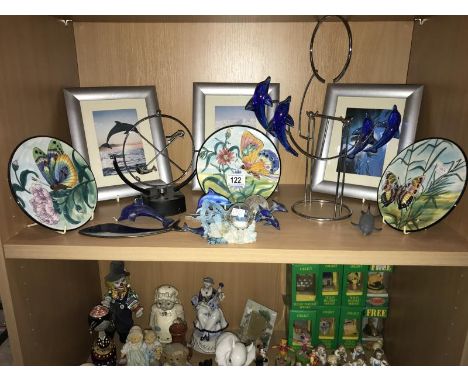 A shelf of miscellaneous. including. animal pictures, butterfly plates, dolphins etc.
