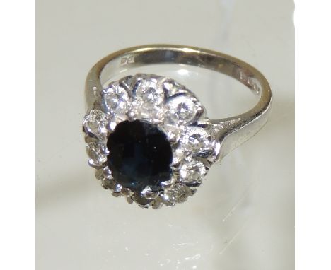 An 18ct white gold sapphire and diamond ring.  Set central oval faceted sapphire with a surround of ten diamonds.  Ring size 