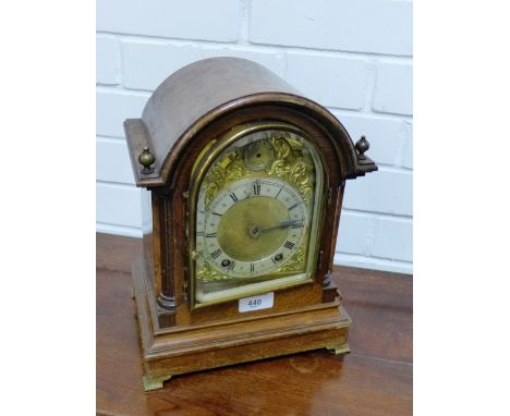 An oak cased mantle clock, the arched top over a brass dial with silvered chapter ring flanked by arm finials, 30 x 25cm