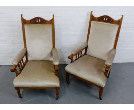 A pair of light oak framed library chairs with pierced and carved top rail over an upholstered back, arms and seats, raised o