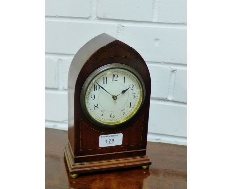 A mahogany and inlaid mantle clock, the arched top over an enameled dial with Arabic numerals, raised on four brass bun feet,