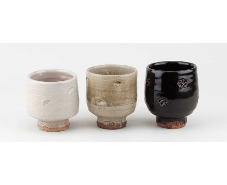 JIM MALONE (born 1946); a trio of stoneware yunomi covered in tenmoku breaking to kaki glaze, green ash glaze and white glaze