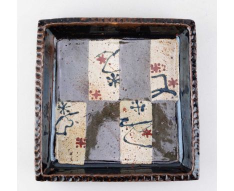 † JOHN MALTBY (1936-2020); a square stoneware dish, the rim covered in tenmoku breaking to kaki glaze, the well decorated wit