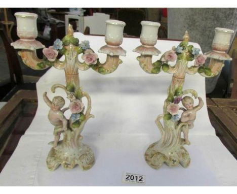 A pair of early 20th century porcelain candlestick surmounted cherubs and with lift off tops.