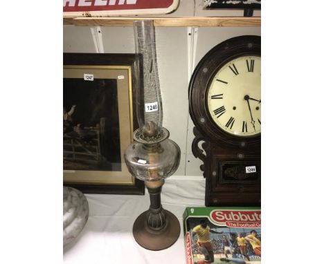 An oil lamp with copper and brass stand, a faceted font and chimney but no shade.