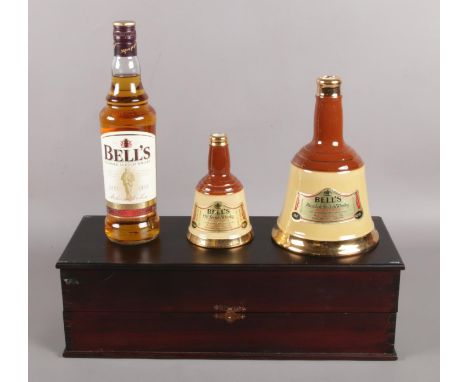 An unopened bottle of Bells Scotch whisky in display case, with two empty ceramic bottles of Bells by Wade.  