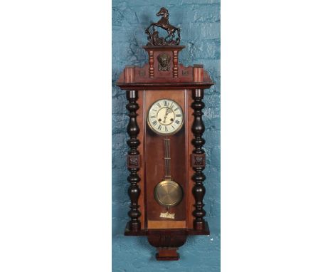 A carved mahogany Vienna wall clock hourly chiming on a coiled gong, the pediment decorated with horse finial and carved mask