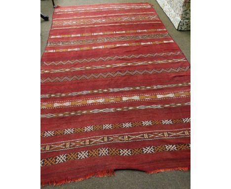 A Moroccan flat weave carpet, North West Africa, the madder field with narrow bands of polychrome geometric designs, 310cm by