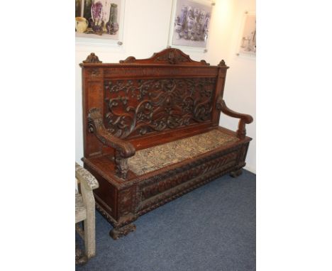 An impressive carved oak settle with high panelled back decorated with griffin, fruiting branches and scrolling foliage benea