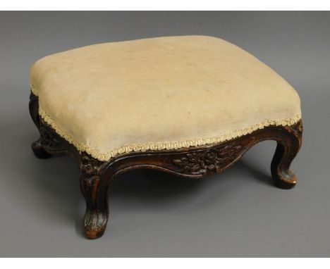 A Victorian upholstered mahogany foot stool with carved decor 