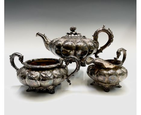 A George IV ornate three-piece silver tea service by Rebecca Emes &amp; Edward Barnard I of melon fluted form with leaf and f