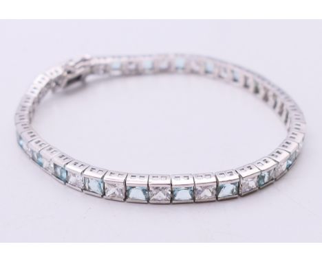 A silver tennis bracelet set with alternating clear and aqua coloured stones. 19 cm long. 