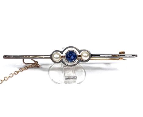 A yellow metal bar brooch set with a central light blue sapphire flanked by two pearls, with safety chain, 3.79gms. 