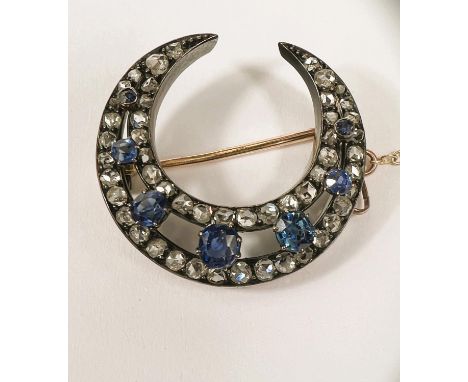 A white and yellow metal crescent brooch with two bands of diamonds with 7 graduating light blue sapphires between, with safe