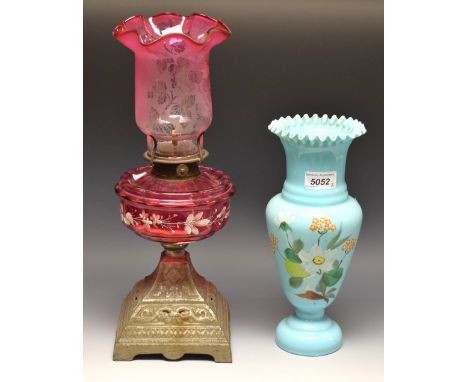 A Victorian Cranberry glass and cast iron paraffin lamp, ornate base, white painted floral reservoir, etched cranberry glass 