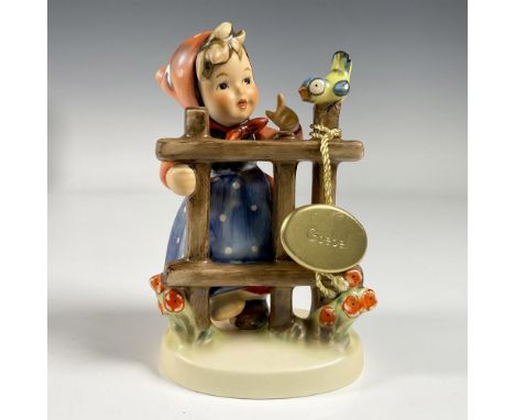 A matte hand painted figure of a girl wearing a polka dotted dress and head scarf, talking to a bird perched on a fence. Fina