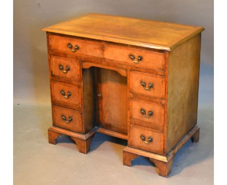 A George III Style Walnut Kneehole Desk, the crossbanded top above seven drawers with brass handles with central kneehole cup