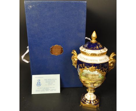 A Coalport Porcelain ' Chatsworth ' Vase and Cover being of ovoid form with rams head handles and acorn finia over shaped squ