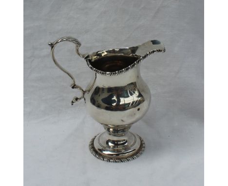 A George III silver cream jug, of urn shape with a gadrooned edge and scrolling handle on a spreading foot, London, 1770, Geo