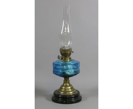 A Victorian brass based oil lamp with blue glass font and chimney.
