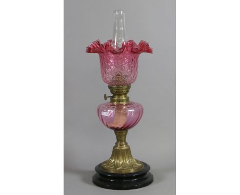 A Victorian brass based oil lamp with coloured glass font and fluted cranberry glass shade and chimney.